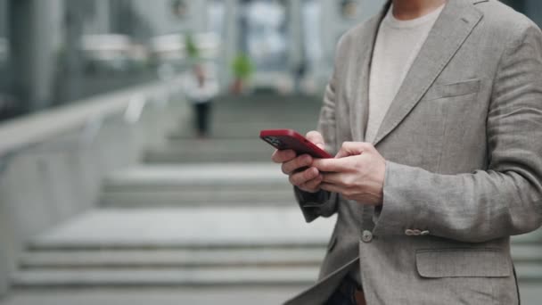 Vista ritagliata del giovane uomo d'affari caucasico fiducioso utilizzando la sua applicazione per smartphone fuori vicino al moderno edificio per uffici. Concetto di persone e tecnologie. — Video Stock