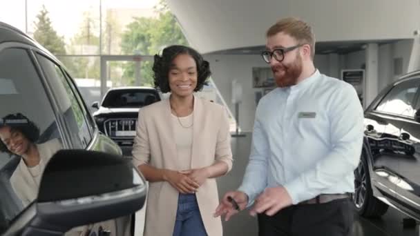 Distribuidor masculino que presenta coche de lujo a cliente femenino africano — Vídeos de Stock