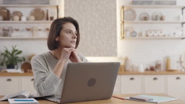 Mulher sentada à mesa com livro e laptop e olhando para longe — Vídeo de Stock