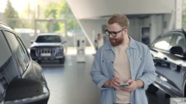 Elinde akıllı telefon olan genç adam yeni bir araba seçiyor.