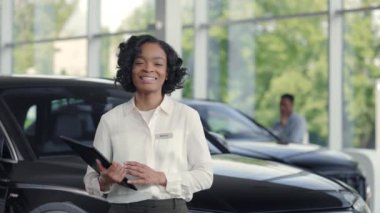 Afrikalı araba satıcısı elinde panoyla sergi salonunda duruyor.