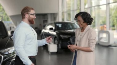 Yeni arabanın anahtarlarını alan ve satıcılarla tokalaşan bir kadın.