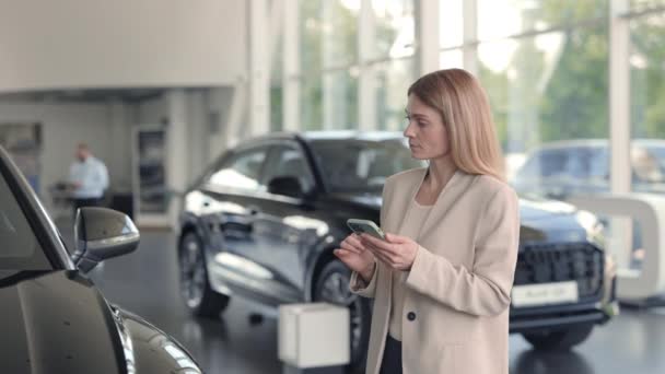 Mujer con smartphone observando auto en concesionario — Vídeo de stock