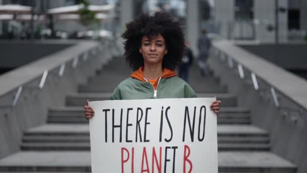 Ecologisch activist. taille omhoog portret uitzicht van de kalme multiraciale meisje staan op de straat en houden banner over onze planeet terwijl het tonen aan de camera. — Stockvideo