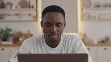 Afrikalı adam dizüstü bilgisayarla masada otururken yan bakıyor.