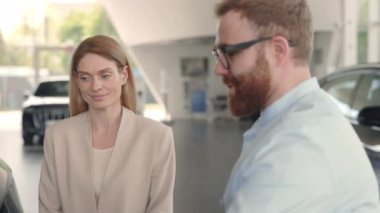 Erkek satıcı kadın alıcıya çeşitli arabalar sunuyor.