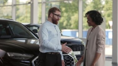Erkek satıcı, araba galerisinde Afrikalı bir kadınla el sıkışıyor.