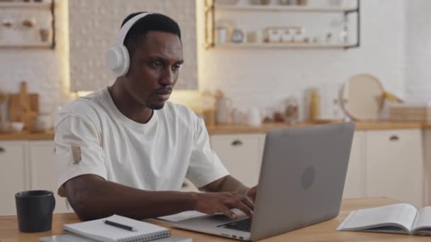 Afrikanischer Student tippt mit Kopfhörern auf Laptop — Stockvideo