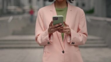 Modern ofis binasının dışında akıllı telefon uygulaması kullanan çok ırklı, kendine güvenen genç iş kadınının görüntüsü. İnsanlar ve teknoloji kavramı.