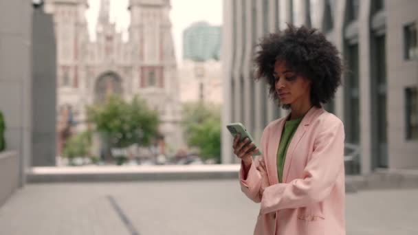 Привлекательная темнокожая молодая элегантная женщина, используя приложение социальных сетей на смартфоне, отправляя сообщения и получая новости, улыбаясь на открытом воздухе. Портреты и технологическая концепция. — стоковое видео