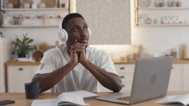 Kulaklıklı dalgın bir adam masada oturuyor ve yan bakıyor.