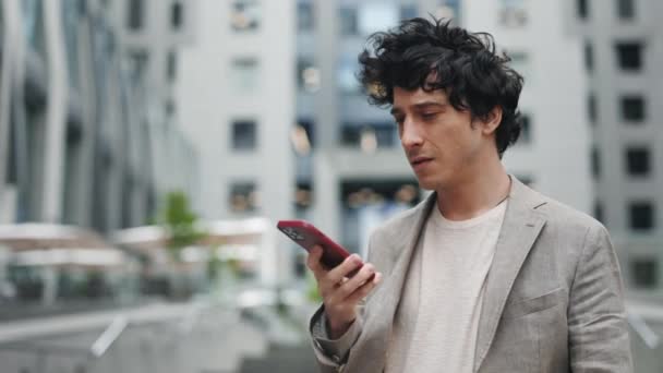 ¿Hola? Hombre guapo sin afeitar de pie en la ciudad y disfrutando de la conversación en su teléfono inteligente. Empresario grabando mensaje de voz para su colega. — Vídeos de Stock