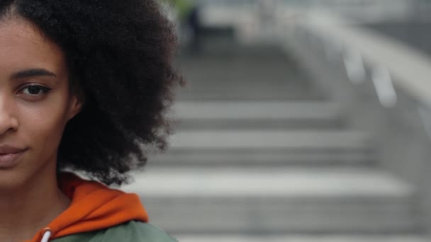 So perfect. Half face portrait of young multiracial brunette woman with curly hair looking at the camera and smiling while standing on blurred background outdoor. — Video Stock