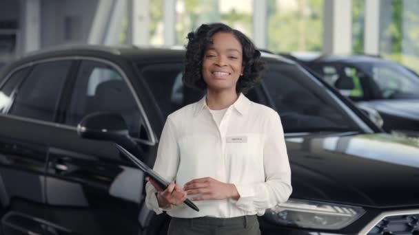 Angenehme Afrikanerin mit Klemmbrett bei der Arbeit im Autosalon — Stockvideo