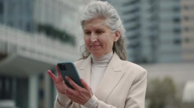 Başarılı, yaşlı kadın, elinde cep telefonuyla dışarıda poz veriyor.
