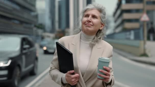 Aged woman with coffee and clipboard walking on street — Stock videók