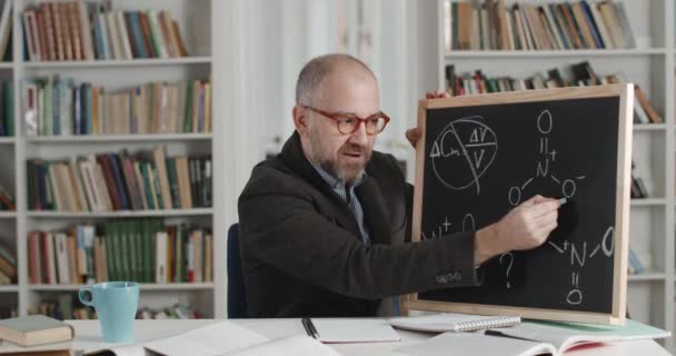 Tutor escribiendo en pizarra mientras lidera la lección de química en línea — Vídeos de Stock