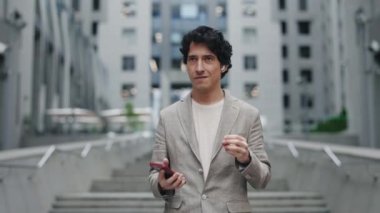 Kafkasyalı iş adamlarının kulaklık takıp, sokakta yürürken ve müzik dinlerken modern akıllı telefon tutmalarını. İş adamları yaşam tarzı kavramı.