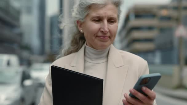 Mujer de negocios de edad avanzada con portapapeles y móvil al aire libre — Vídeos de Stock