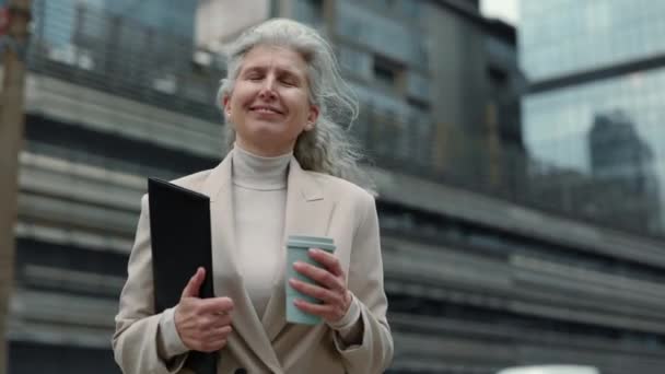 通りにクリップボードとコーヒーを運ぶ高齢者のビジネス女性 — ストック動画