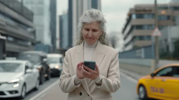 Yaşlı iş kadını sokakta cep telefonuyla kayıt yapıyor. — Stok video