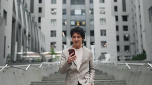 Uomo caucasico sorridente che indossa un abito formale usando il telefono cellulare e registrando messaggi vocali mentre cammina fuori dal centro commerciale e corre giù per le scale. Tecnologie e concetto di persone. — Video Stock