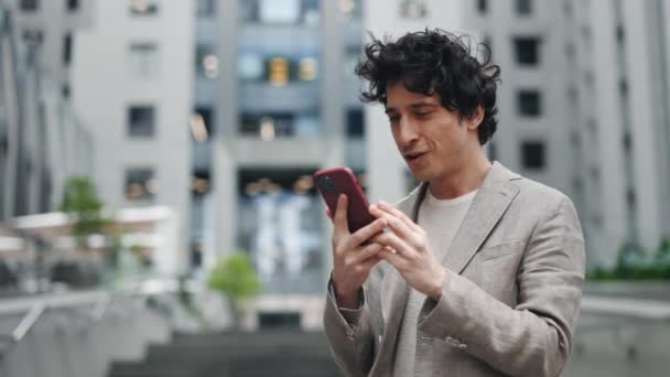 Feliz hombre de negocios disfrutando del éxito en el teléfono inteligente de pie cerca del centro de oficinas. Hombre leyendo buenas noticias en el teléfono en cámara lenta. Sorprendido hombre celebrando la victoria por teléfono en la ciudad. — Vídeo de stock