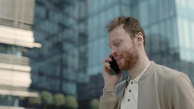 Şık giyinen adam sokakta yürüyor ve cep telefonuyla konuşuyor.