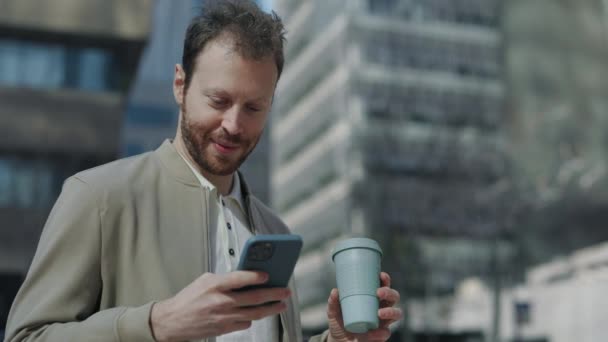 Бизнесмен пьет кофе и пользуется мобильным телефоном на улице — стоковое видео