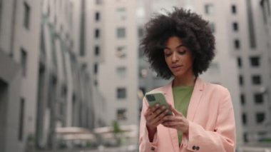Yetişkin, çok ırklı, kendine güvenen iş kadınının resmi giyinmiş portresi modern ofis binasının yakınındaki telefonuna mesaj atıyor. Hareket kamerasıyla kurumsal çekim.