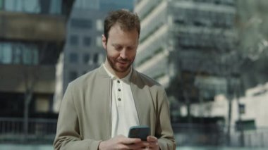Yakışıklı adam sokakta dikiliyor ve akıllı telefon kullanıyor.