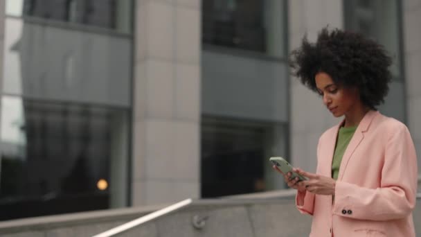Krásná mladá podnikatelka ve formálním obleku a pomocí moderního chytrého telefonu při procházce po městě. Profesionální zaměstnavatelka psaní textové zprávy na mobilní telefon venku. — Stock video
