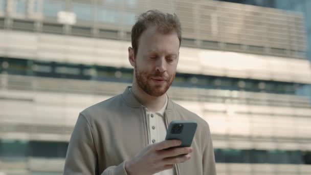 Homem atraente usando smartphone enquanto está de pé na rua — Vídeo de Stock