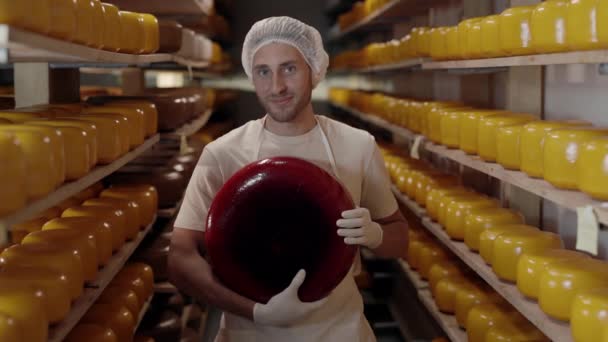 Jeune homme debout à la ferme laitière avec la tête de fromage dans les mains — Video