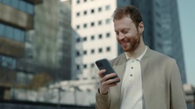 Gülümseyen işadamı sokakta yürürken akıllı telefon kullanıyor.