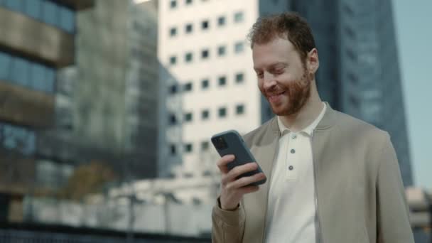 Улыбающийся бизнесмен с помощью смартфона во время прогулки по улице — стоковое видео