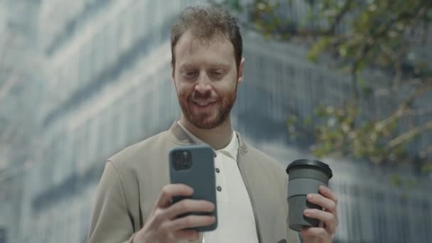 Счастливый человек стоит на улице и смотрит на мобильный экран — стоковое видео