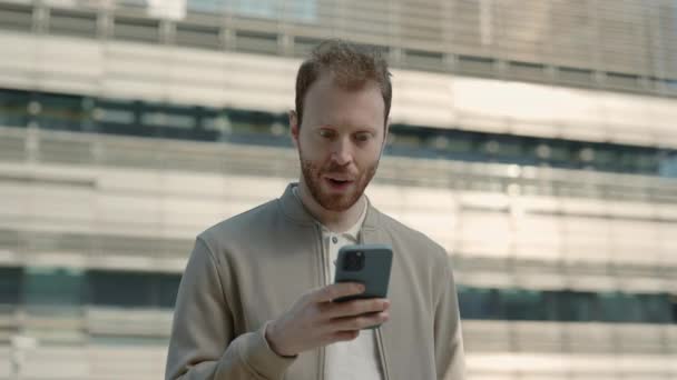 Удивленный бизнесмен, стоящий на улице с мобильным телефоном в руке — стоковое видео