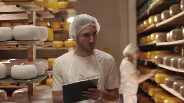 Homem e mulher trabalhando na fazenda de laticínios com cabeças de queijo — Vídeo de Stock