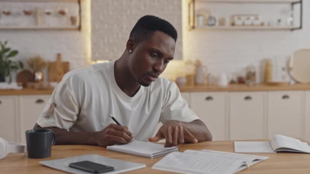 Man reading book and taking notes while studying at home — Stockvideo