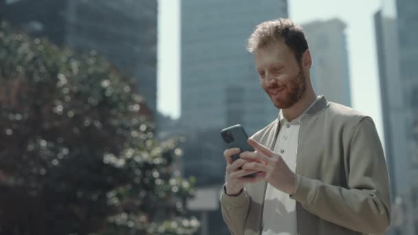 Brodaty biznesmen stojący na zewnątrz i korzystający z telefonu komórkowego — Wideo stockowe