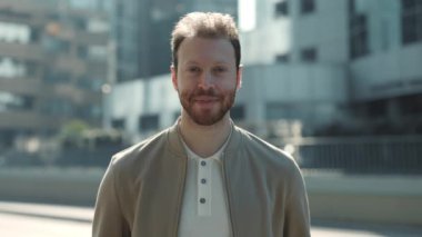 Yakışıklı sakallı adam şık giyinmiş, açık havada duruyor.