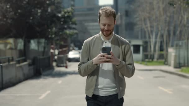 Бородач ходит по улице и пишет смс по мобильному. — стоковое видео