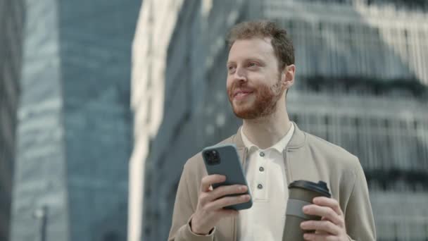 Erkek girişimci kahve ve cep telefonuyla caddede duruyor. — Stok video