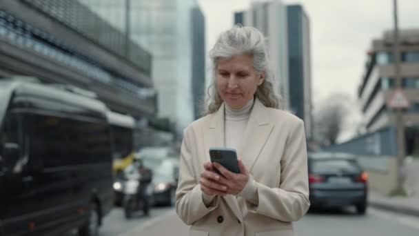 Zakelijke vrouw met grijs haar met behulp van mobiele telefoon op stree — Stockvideo