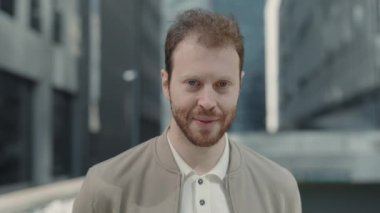 Kendine güvenen işadamı modern ofis binalarının arka planındaki caddede duran kameraya bakıyor. İnsan kavramı, iş ve başarılı kariyer.