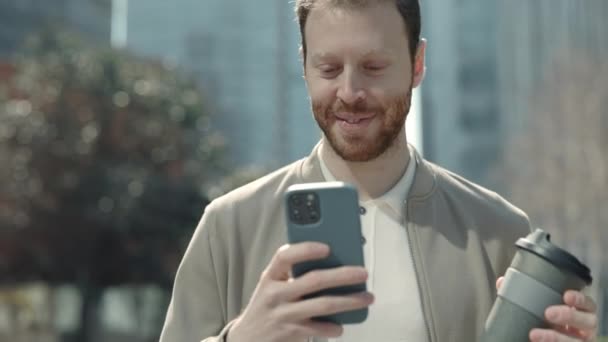 Красивый человек с чашкой кофе с помощью смартфона на открытом воздухе — стоковое видео