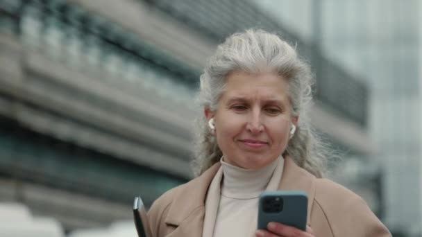 Mujer de negocios que lleva portapapeles y mensajes de texto en el móvil — Vídeos de Stock