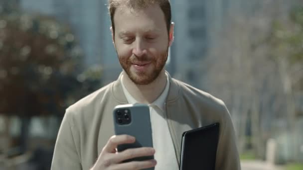 Бизнесмен с мобильным телефоном и планшетом идет по улице — стоковое видео