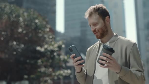 Mannelijke ondernemer staat op straat met mobiele en koffie — Stockvideo